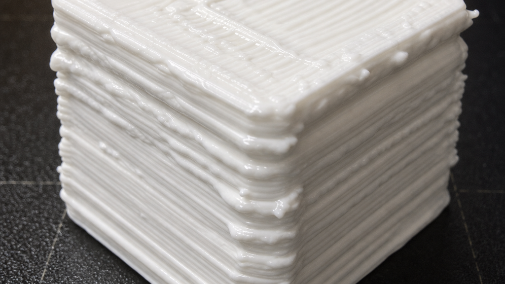Close-up of a white cube with swollen rounded corners and heavy ridges from excess material flow.