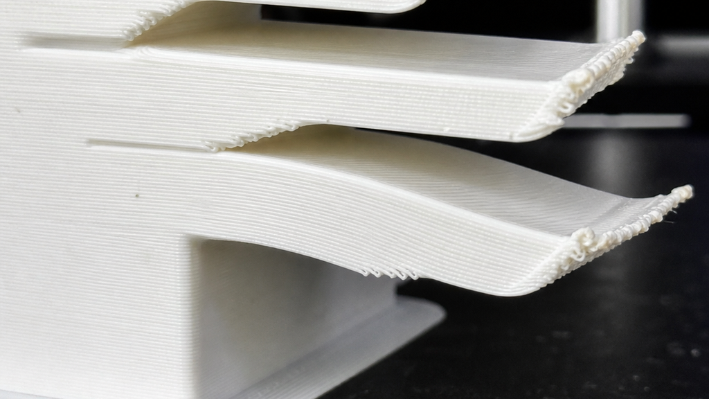 Unsupported white overhang edges curling upward with rough tips.